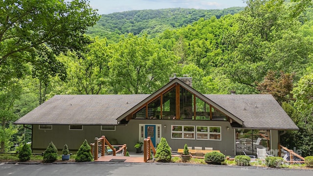 rear view of property with roof with shingles, an outdoor living space, a deck, and a wooded view