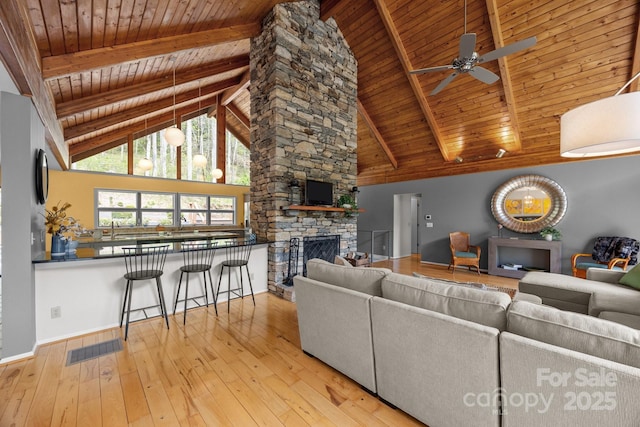living room featuring a stone fireplace, ceiling fan, wooden ceiling, wood-type flooring, and visible vents