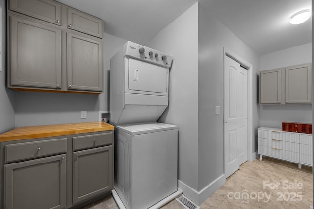 washroom with stacked washer and clothes dryer, baseboards, and cabinet space
