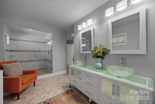 bathroom featuring double vanity, a shower stall, baseboards, and a sink