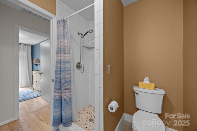 bathroom with toilet, wood finished floors, baseboards, and a tile shower
