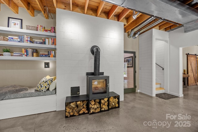 unfurnished living room featuring stairs, concrete block wall, finished concrete flooring, and a wood stove