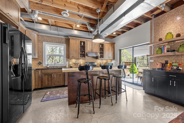 kitchen with a sink, tasteful backsplash, black fridge with ice dispenser, under cabinet range hood, and a kitchen island