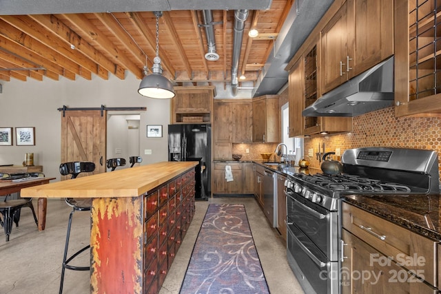 kitchen with a barn door, butcher block counters, stainless steel appliances, finished concrete flooring, and under cabinet range hood