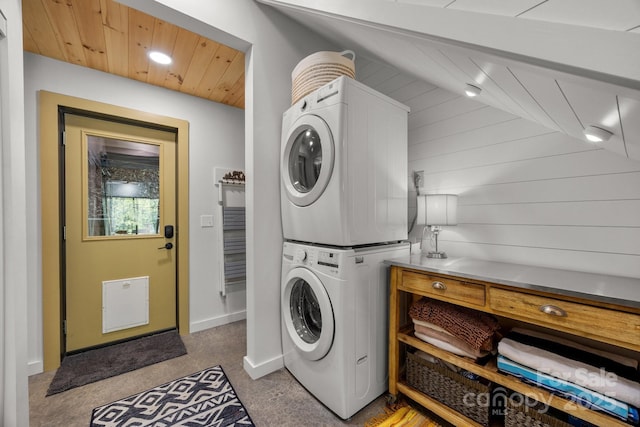 laundry area featuring carpet floors, stacked washer / drying machine, wooden ceiling, baseboards, and laundry area