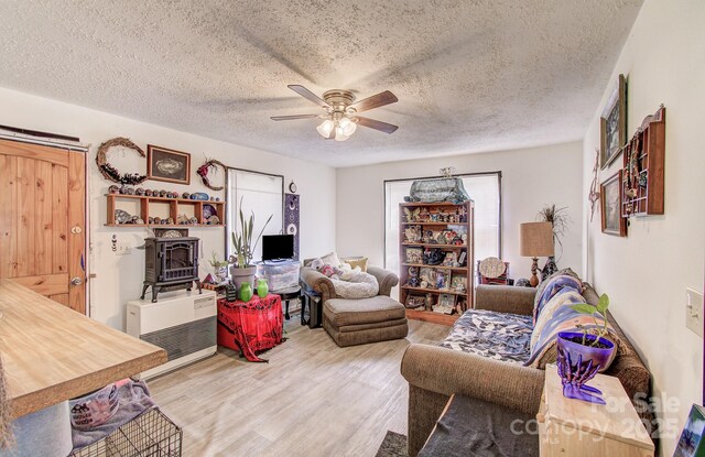 living area with a textured ceiling, light wood-style floors, a wood stove, and ceiling fan