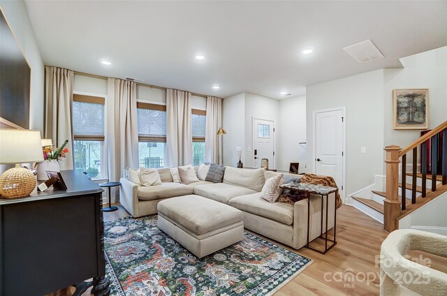 living area with recessed lighting, light wood finished floors, and stairs