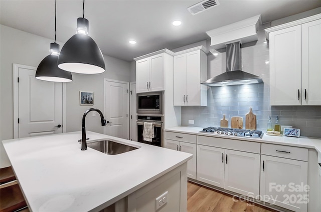 kitchen featuring backsplash, a sink, visible vents, appliances with stainless steel finishes, and wall chimney exhaust hood