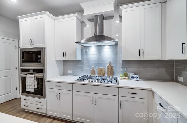 kitchen with light countertops, wall chimney range hood, wood finished floors, and appliances with stainless steel finishes