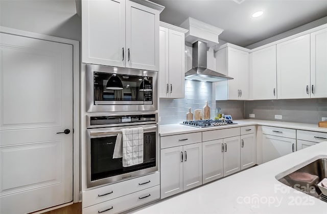 kitchen featuring light countertops, stainless steel gas cooktop, decorative backsplash, and wall chimney exhaust hood