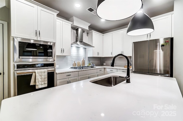 kitchen featuring light countertops, stainless steel appliances, decorative backsplash, a sink, and wall chimney exhaust hood