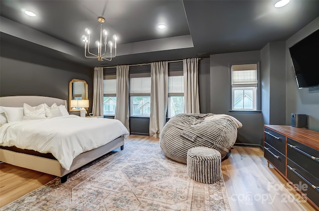 bedroom with a tray ceiling, light wood-style flooring, recessed lighting, and a notable chandelier