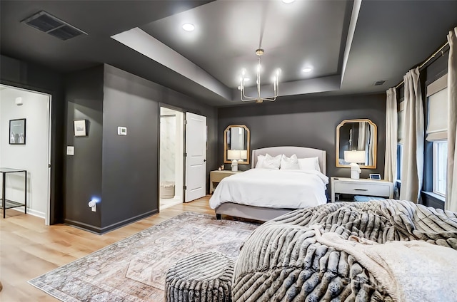 bedroom with a tray ceiling, visible vents, and light wood finished floors