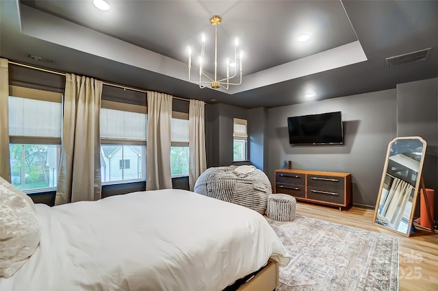 bedroom with visible vents, recessed lighting, a raised ceiling, light wood-type flooring, and an inviting chandelier