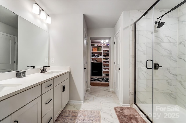 full bath with a sink, a shower stall, a walk in closet, marble finish floor, and baseboards