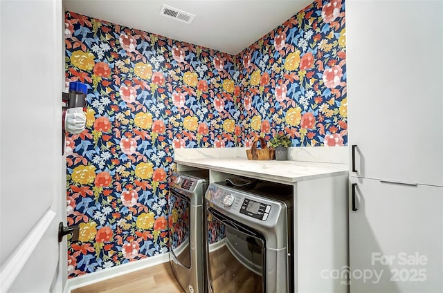 clothes washing area featuring visible vents, wood finished floors, laundry area, wallpapered walls, and washer and clothes dryer