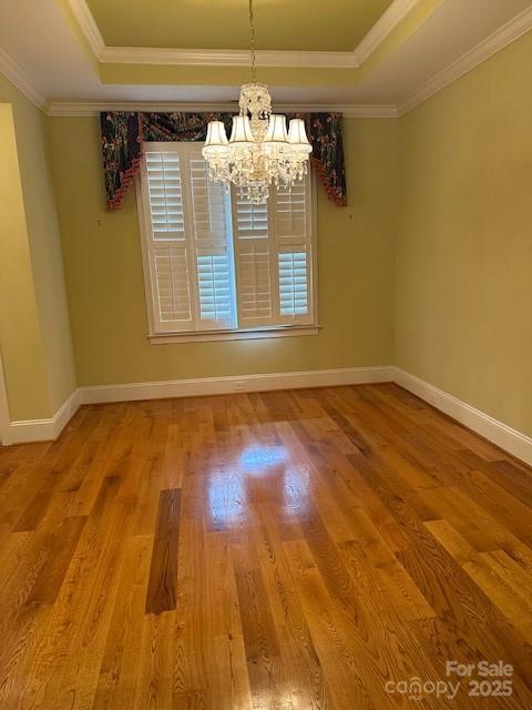unfurnished dining area with wood finished floors, a raised ceiling, crown molding, and a chandelier