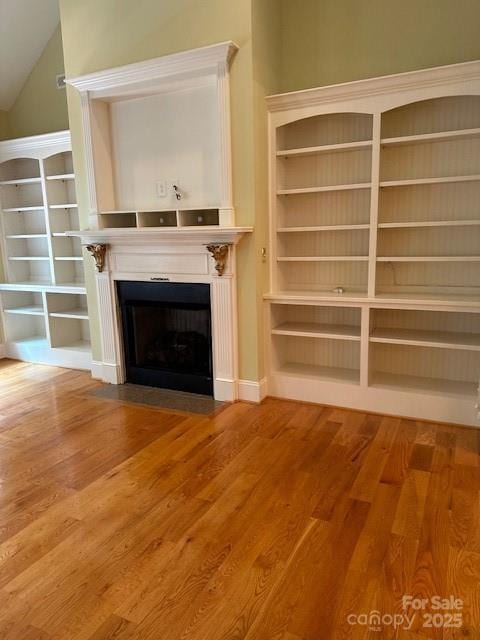 unfurnished living room featuring wood finished floors, a fireplace with flush hearth, and vaulted ceiling