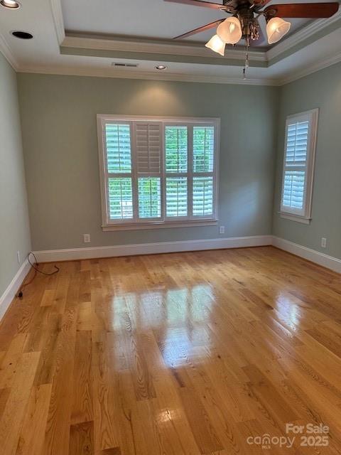 empty room featuring light wood-type flooring, a raised ceiling, ceiling fan, and ornamental molding