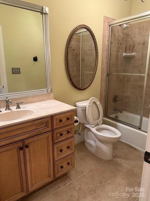 bathroom featuring toilet, combined bath / shower with glass door, vanity, and tile patterned flooring