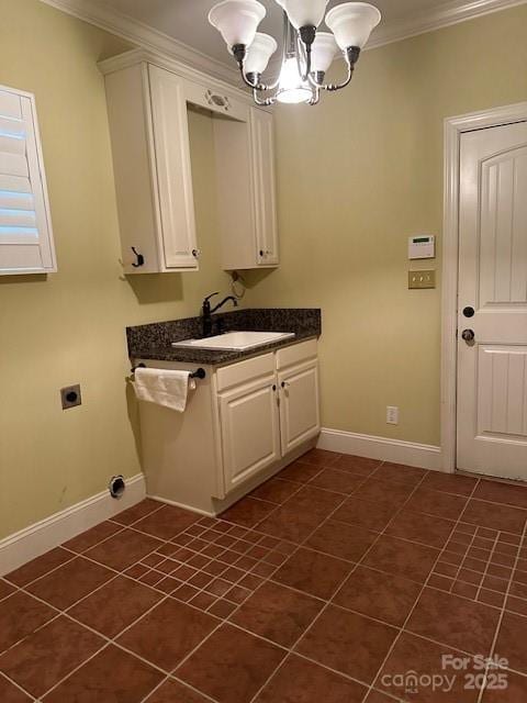 laundry area featuring dark tile patterned floors, a sink, baseboards, a notable chandelier, and crown molding