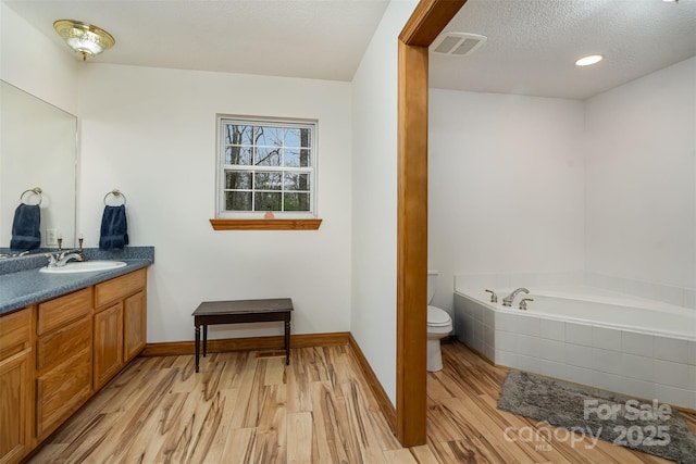 bathroom featuring visible vents, toilet, vanity, wood finished floors, and a garden tub