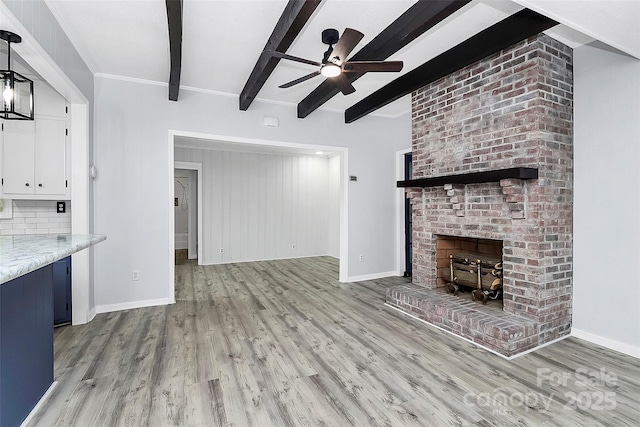unfurnished living room featuring beam ceiling, a fireplace, light wood-style flooring, baseboards, and ceiling fan