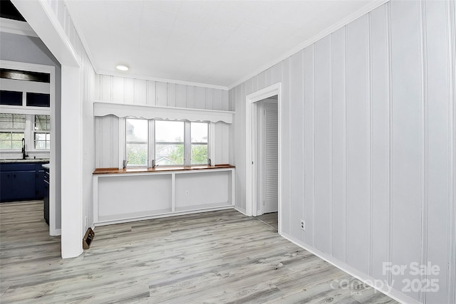 empty room featuring a sink, ornamental molding, and light wood-type flooring
