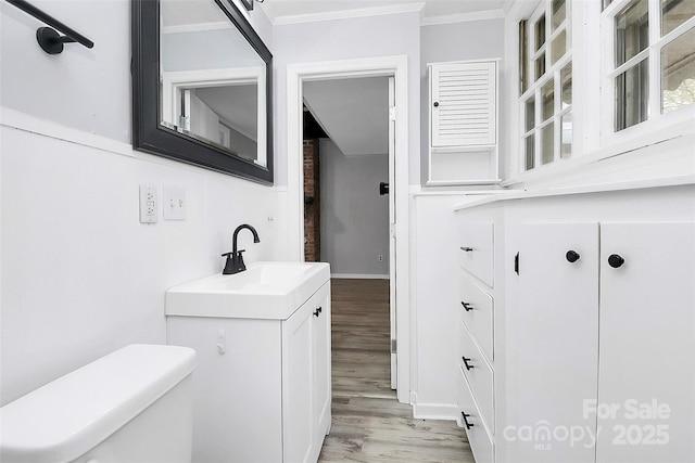 bathroom with toilet, wood finished floors, vanity, and ornamental molding