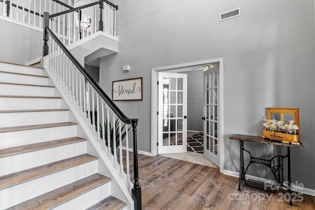 staircase with french doors, wood finished floors, baseboards, and visible vents