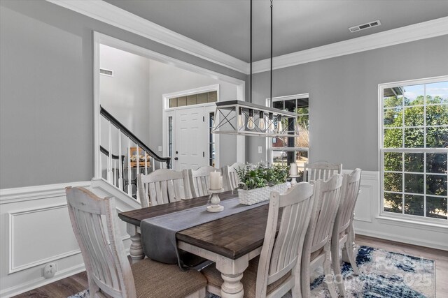 dining room with wainscoting, visible vents, a decorative wall, and crown molding