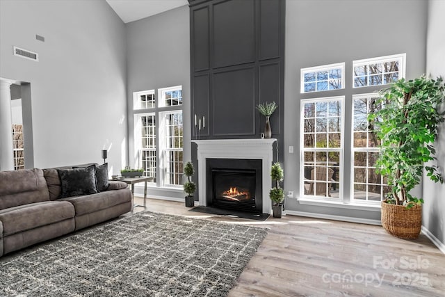 living area with a towering ceiling, a large fireplace, plenty of natural light, visible vents, and wood finished floors