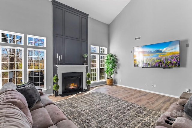 living area with visible vents, baseboards, high vaulted ceiling, and wood finished floors