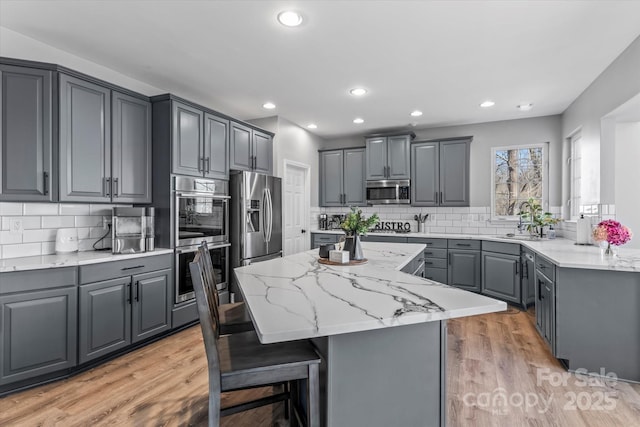 kitchen featuring stainless steel appliances, gray cabinets, light stone countertops, a center island, and tasteful backsplash