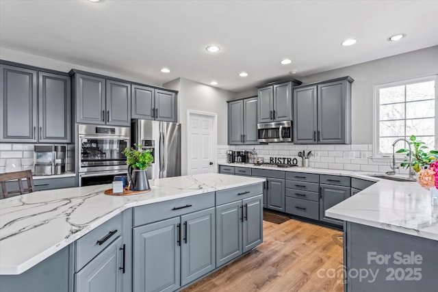 kitchen featuring light stone counters, a sink, decorative backsplash, gray cabinets, and appliances with stainless steel finishes