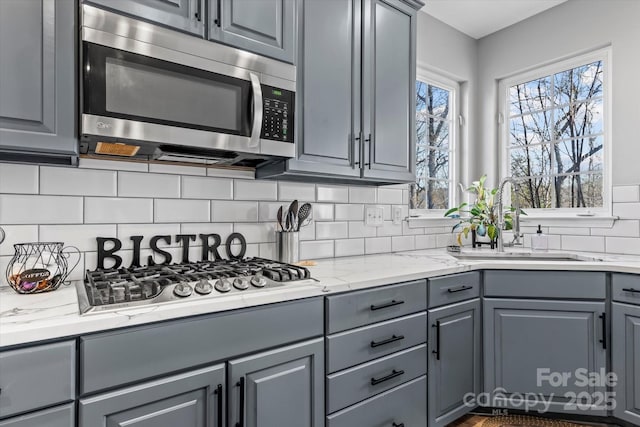 kitchen with stainless steel appliances, gray cabinetry, a sink, and decorative backsplash