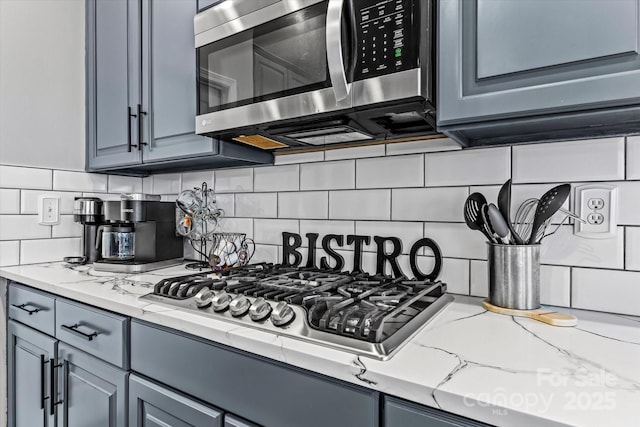 kitchen with backsplash, light stone countertops, appliances with stainless steel finishes, and gray cabinetry