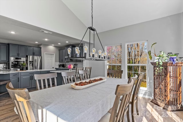 dining space with a towering ceiling, wood finished floors, visible vents, and recessed lighting
