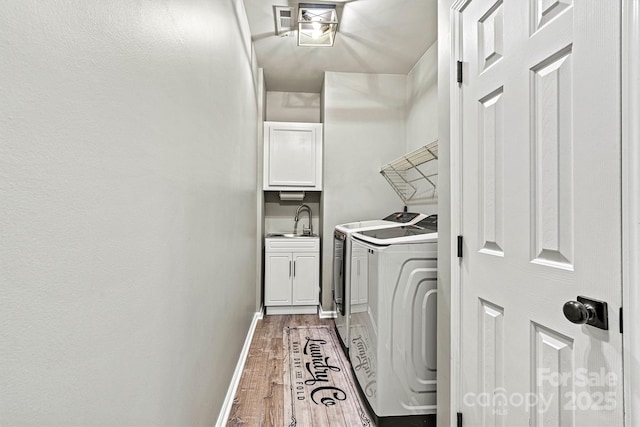 clothes washing area featuring a sink, baseboards, wood finished floors, cabinet space, and washer and dryer