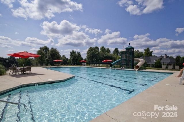 community pool with fence, a water slide, and a patio