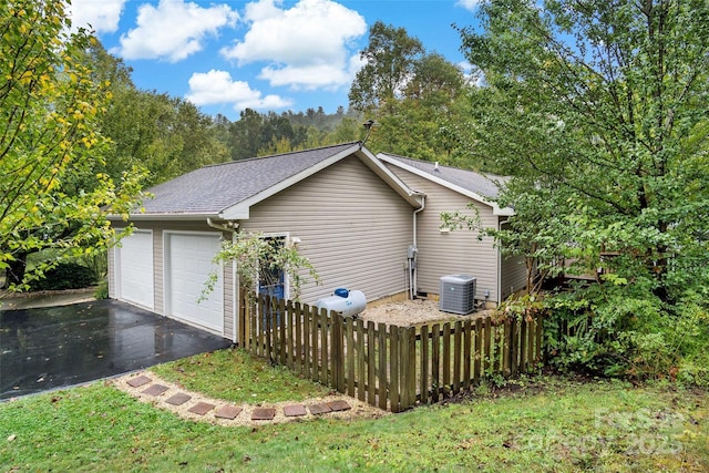 view of side of home featuring fence, aphalt driveway, a shingled roof, central AC unit, and a garage