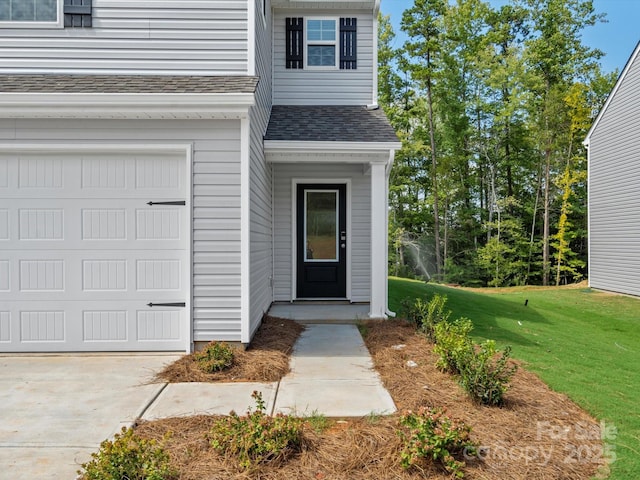 entrance to property with concrete driveway, a shingled roof, and a yard