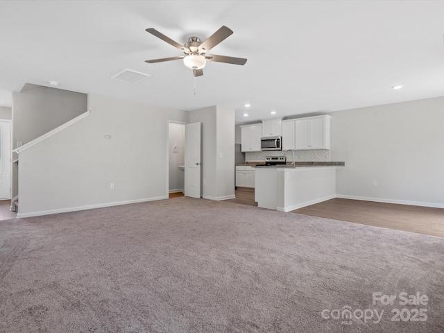 unfurnished living room with light colored carpet, visible vents, baseboards, and a ceiling fan
