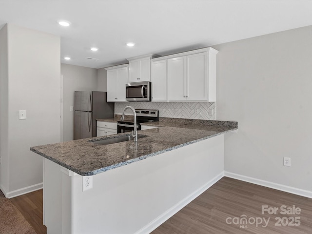 kitchen with a sink, backsplash, appliances with stainless steel finishes, dark wood-style floors, and white cabinets