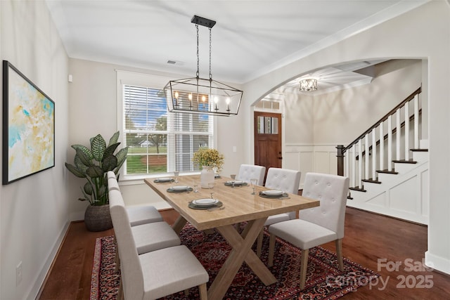 dining space with dark wood-style flooring, visible vents, arched walkways, a notable chandelier, and ornamental molding