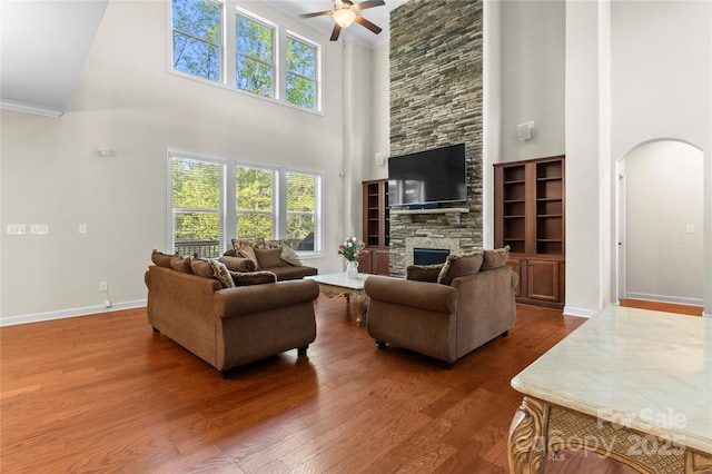 living room featuring a high ceiling, arched walkways, ceiling fan, crown molding, and wood finished floors