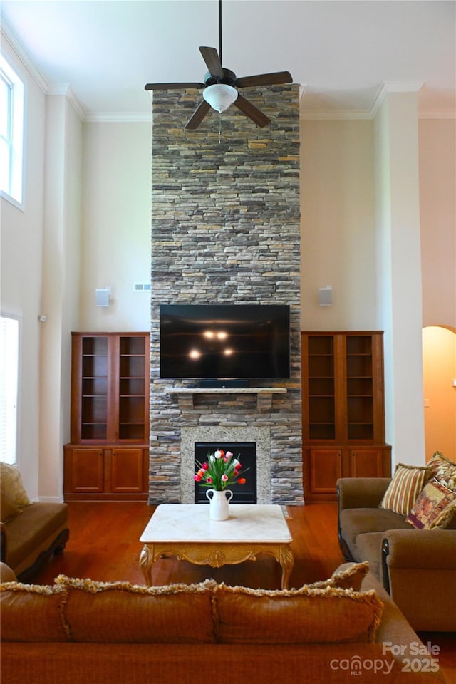 living area with ceiling fan, wood finished floors, a fireplace, ornamental molding, and arched walkways