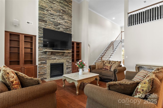 living room featuring crown molding, wood finished floors, stairs, a high ceiling, and a fireplace