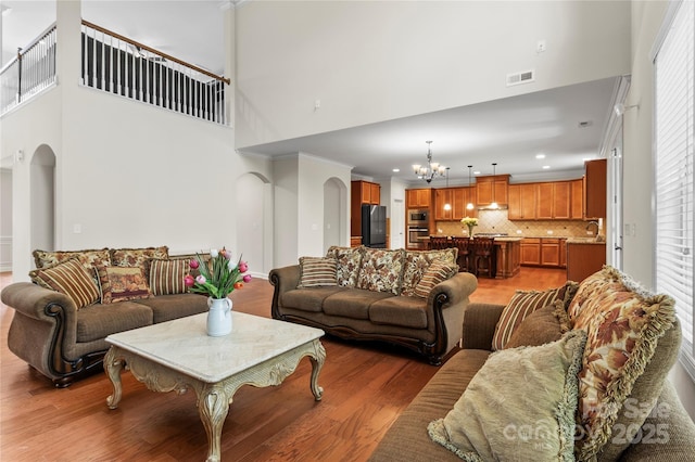 living room with a chandelier, arched walkways, a high ceiling, light wood-type flooring, and recessed lighting
