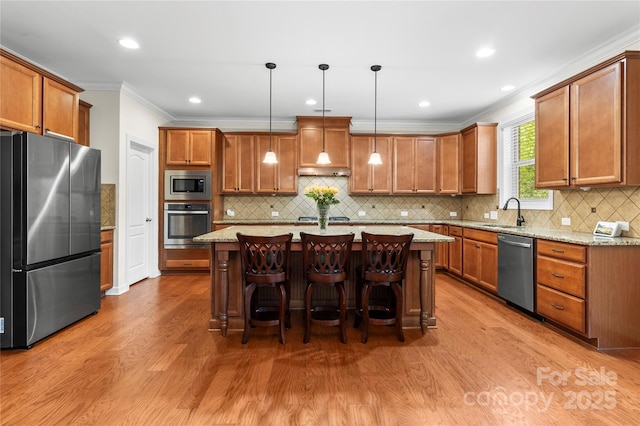 kitchen with appliances with stainless steel finishes, wood finished floors, brown cabinetry, crown molding, and light stone countertops